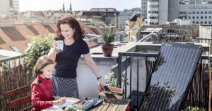 Frau mit Kind auf einem Balkon, der mit einem PV-Modul "Simon" ausgestatttet ist.