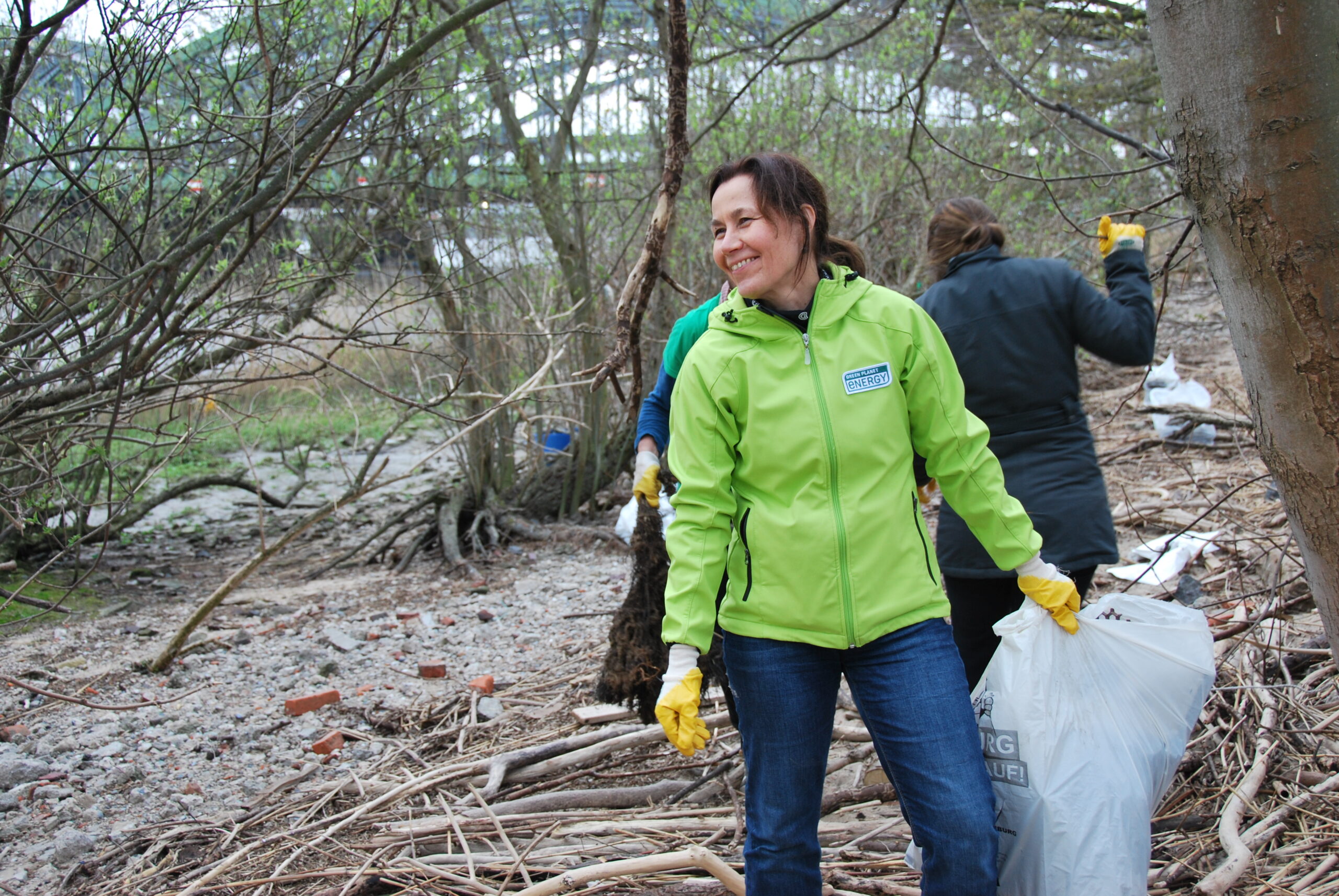 Eine Mitarbeiterin von Green Planet Energy hält einen Müllsack in der Hand und lacht in die Kamera.