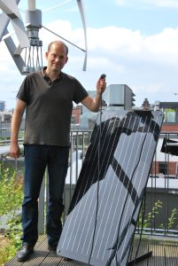 Green Planet Energy-Vorstand Sönke Tangermann mit dem Balkon-PV-Modul "simon" auf dem mit Windkraft- und Solaranlagen bestückten GPE-Dach.